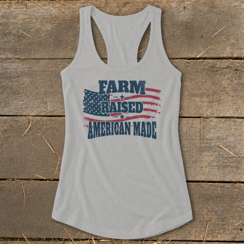 Light gray racerback tank top with distressed American flag graphic and "FARM RAISED AMERICAN MADE" text.