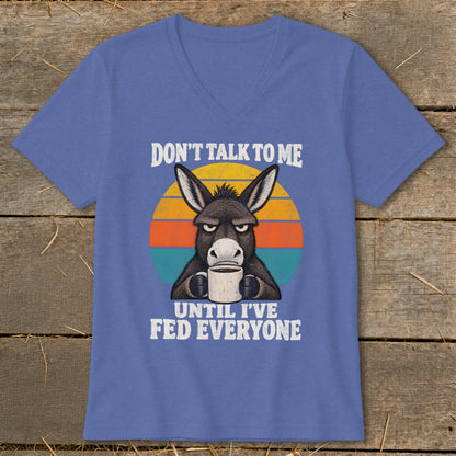 Blue V-neck t-shirt featuring a graphic of a grumpy donkey holding a coffee mug and text reading Don't Talk to Me Until I've Fed Everyone.