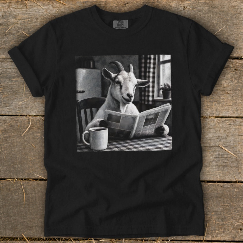 A black t-shirt features a black and white graphic of a goat sitting at a table, reading a newspaper next to a coffee mug.