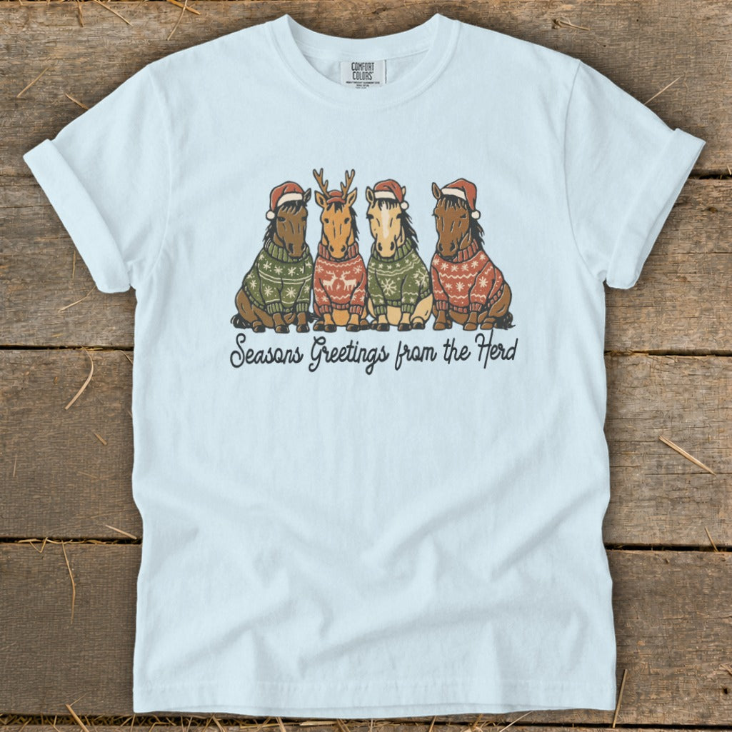 Light blue t-shirt with four horses in Christmas sweaters and Santa hats, reading "Seasons Greetings from the Herd".