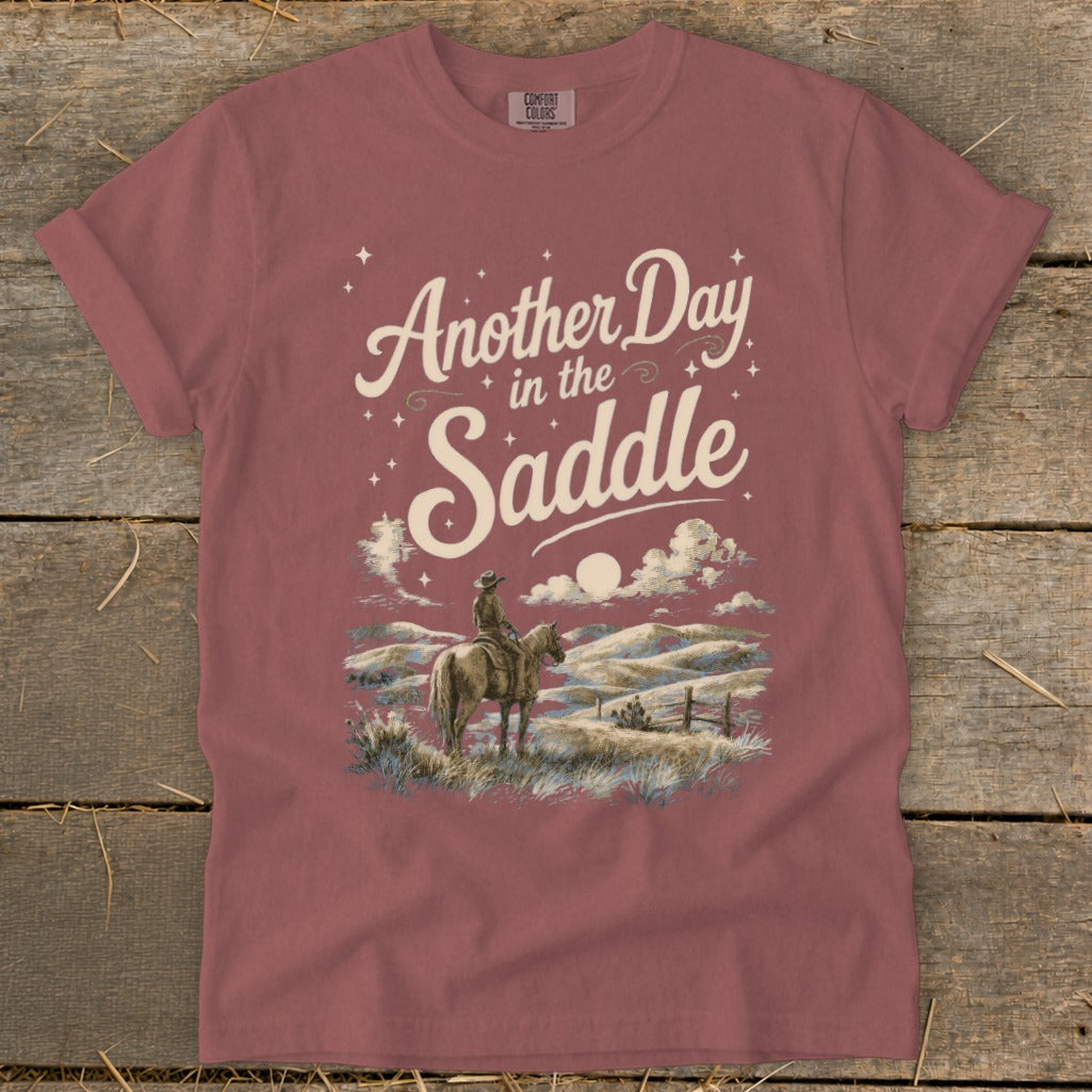 T-shirt graphic: "Another Day in the Saddle" with cowboy on horseback, scenic landscape.