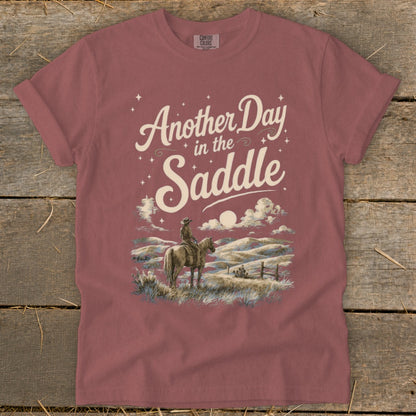 T-shirt graphic: "Another Day in the Saddle" with cowboy on horseback, scenic landscape.