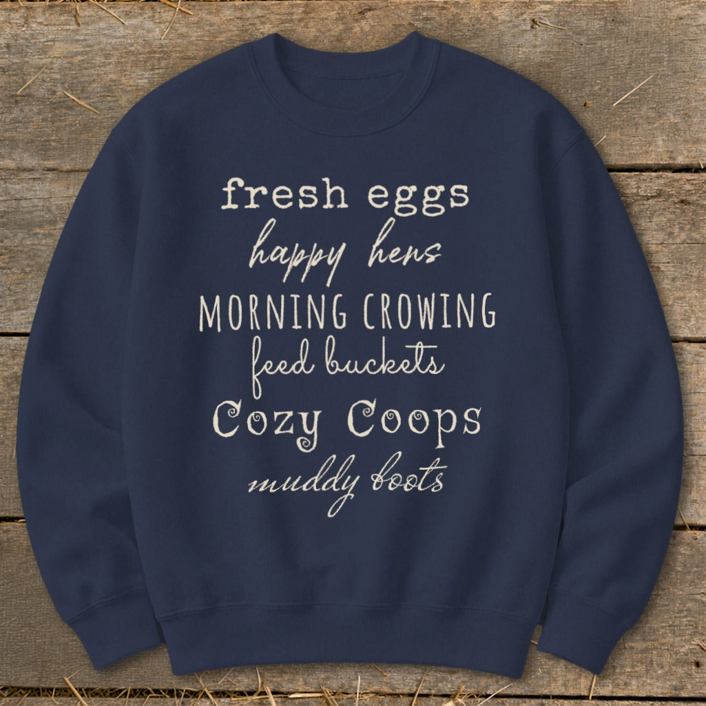 Navy sweatshirt with white text listing "fresh eggs," "happy hens," "morning crowing," "feed buckets," "cozy coops," and "muddy boots."