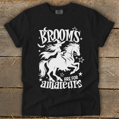 Black t-shirt with white graphic of witch riding horse, text "Brooms are for amateurs."