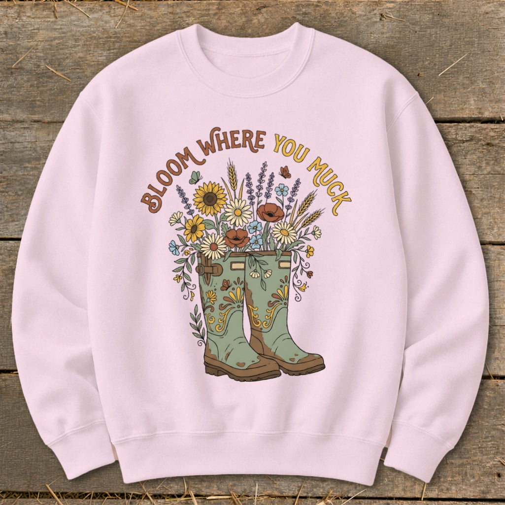 Pink sweatshirt with illustration of green boots overflowing with flowers and text "Bloom Where You Muck".