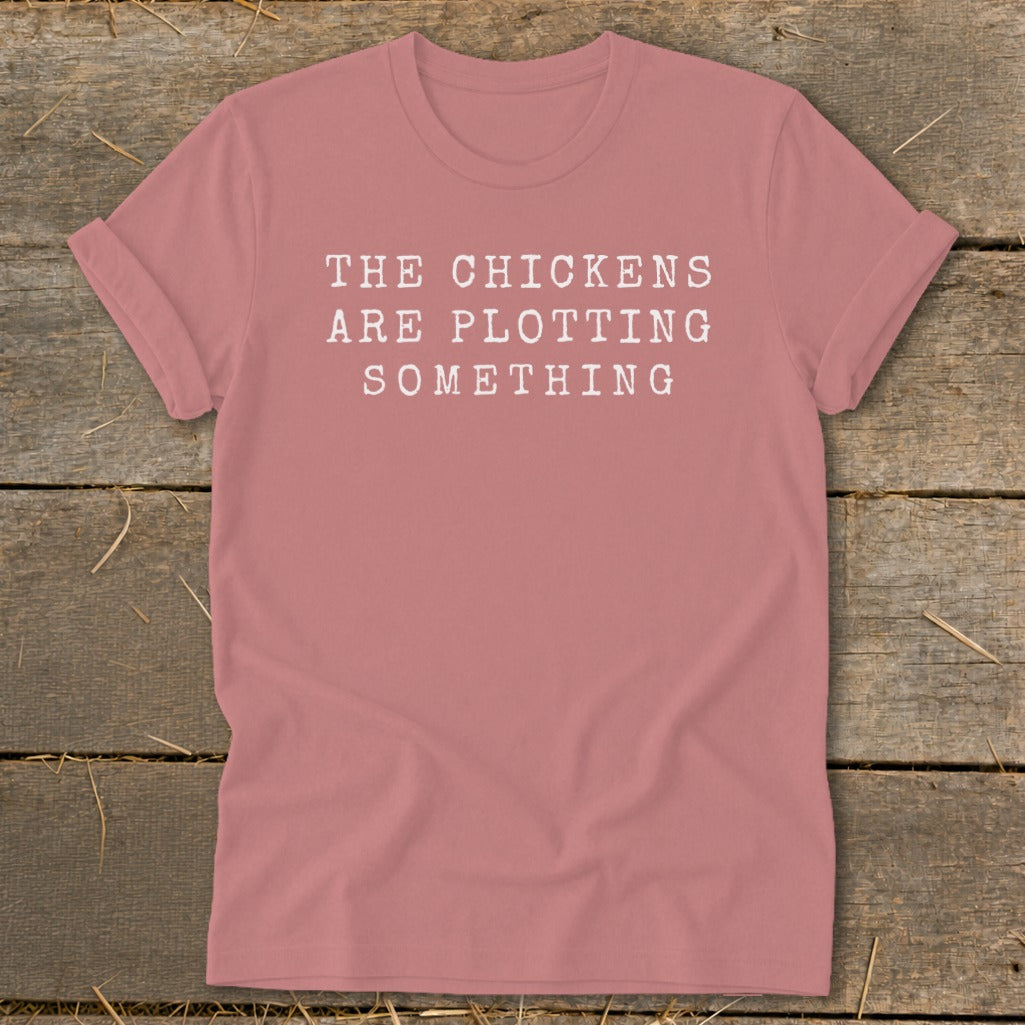 Rose t-shirt with white text reading "THE CHICKENS ARE PLOTTING SOMETHING".