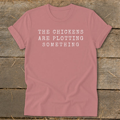 Rose t-shirt with white text reading "THE CHICKENS ARE PLOTTING SOMETHING".