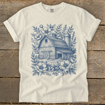 White t-shirt with blue sketch of a barn, silo, fence, and flowers.