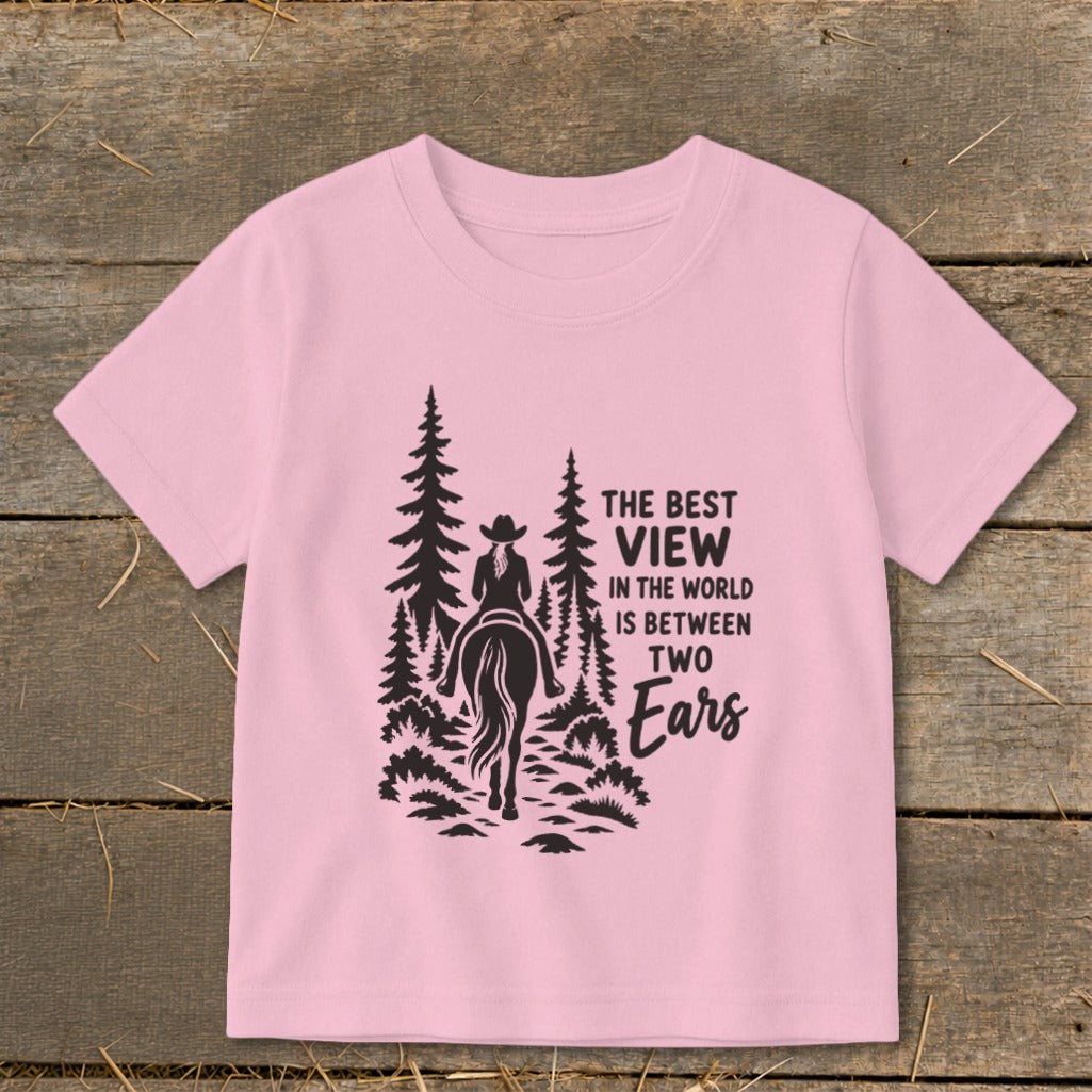 A pink t-shirt featuring a black graphic of a horseback rider among trees and text.
