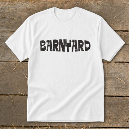 A white crewneck t-shirt lies flat on a rustic wooden surface, featuring the black distressed text BARNYARD centered on the chest.