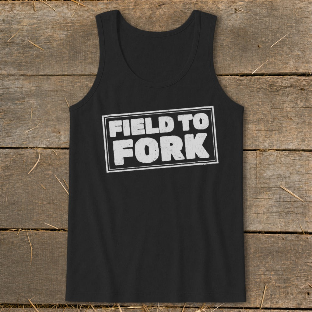 A black tank top with the white distressed text "FIELD TO FORK" centered on a rustic wooden background.