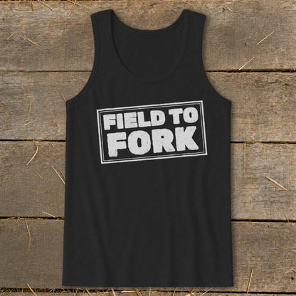 A black tank top with the white distressed text "FIELD TO FORK" centered on a rustic wooden background.