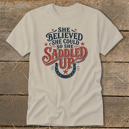 Cream t-shirt with "She Believed She Could So She Saddled Up" text and horseshoe graphic.