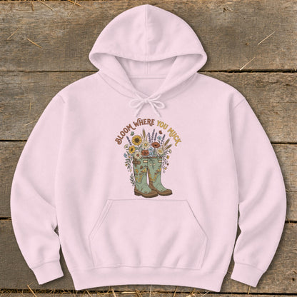 Pink hoodie with "Bloom Where You Muck" text and floral design in rain boots.