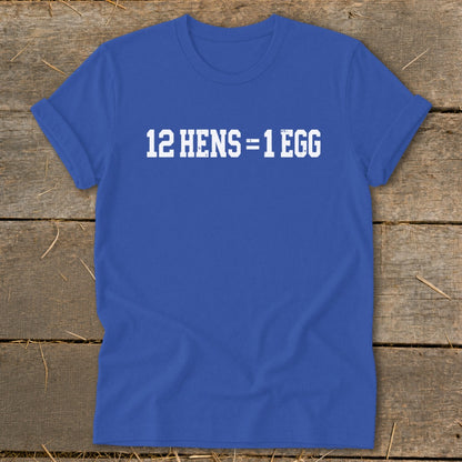 Royal blue short-sleeve t-shirt with white distressed text reading 12 HENS = 1 EGG laid flat on a rustic wooden background.