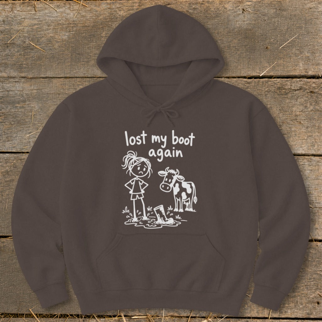 Dark brown hoodie featuring a white cartoon graphic of a sad girl and a cow standing near a muddy boot with the text "lost my boot again."