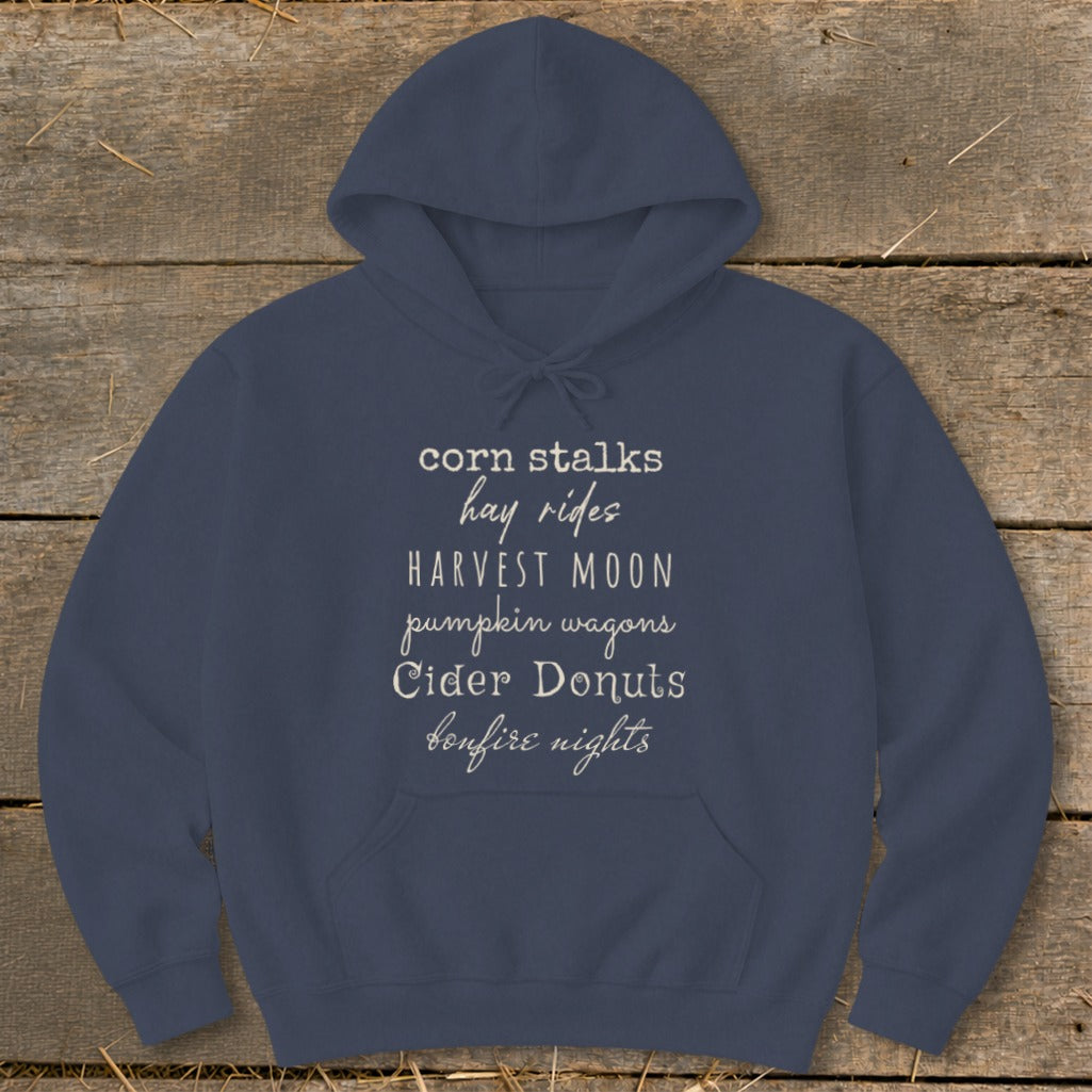 Navy hoodie with fall-themed text: corn stalks, hay rides, harvest moon, pumpkin wagons, cider donuts, bonfire nights.