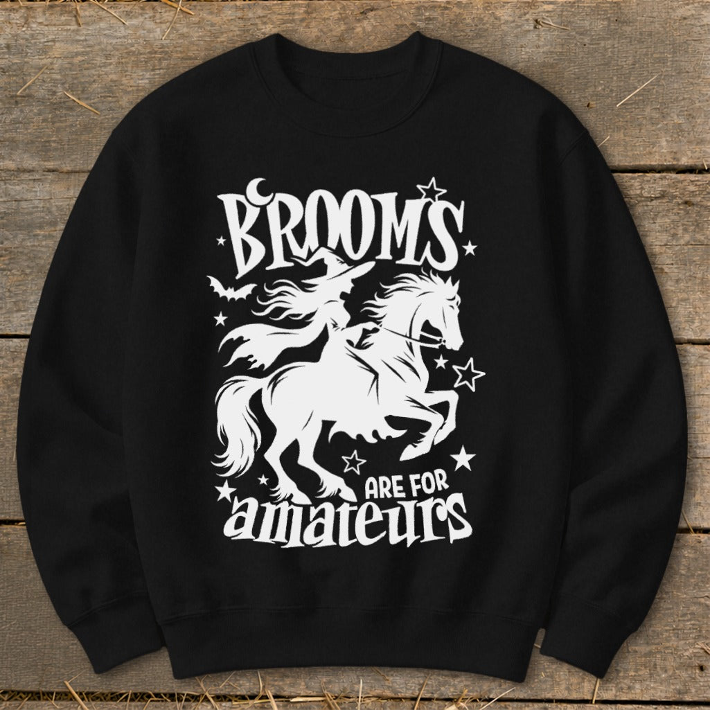White graphic on black sweatshirt shows witch riding horse with text "BROOMS ARE FOR amateurs".