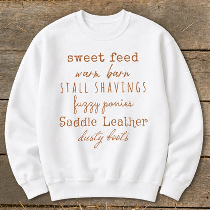 White sweatshirt with "sweet feed warm barn stall shavings fuzzy ponies Saddle Leather dusty boots" text.