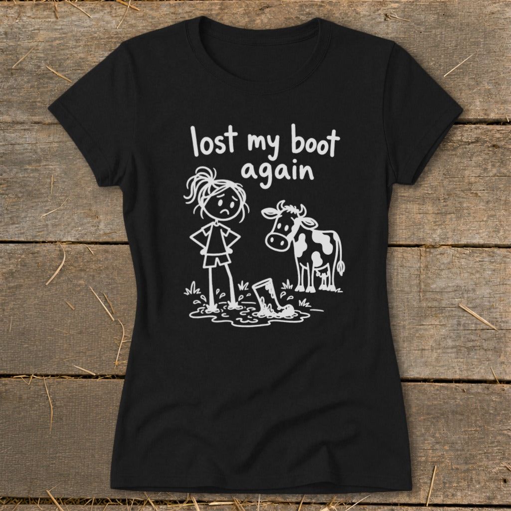 Black t-shirt featuring a white graphic of a sad girl standing next to a cow near a muddy boot, with text reading lost my boot again.