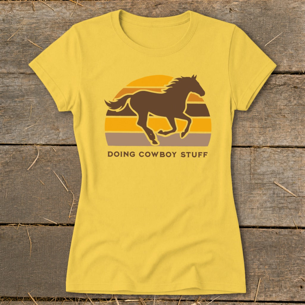 Yellow t-shirt with a dark brown horse silhouette against a sunset and text "DOING COWBOY STUFF".