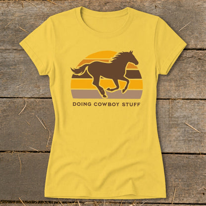 Yellow t-shirt with a dark brown horse silhouette against a sunset and text "DOING COWBOY STUFF".