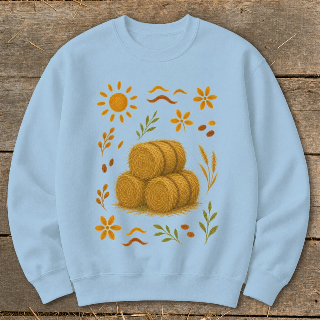 Light blue sweatshirt with stacked hay bales and autumn leaf, sun, and flower motifs.
