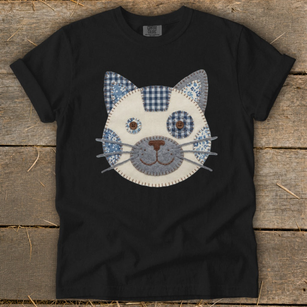 Black t-shirt with a fabric cat face applique featuring blue and white patterns.