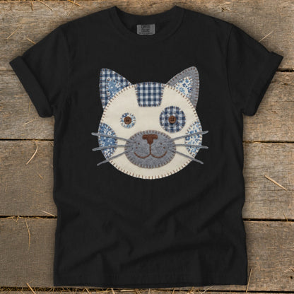 Black t-shirt with a fabric cat face applique featuring blue and white patterns.