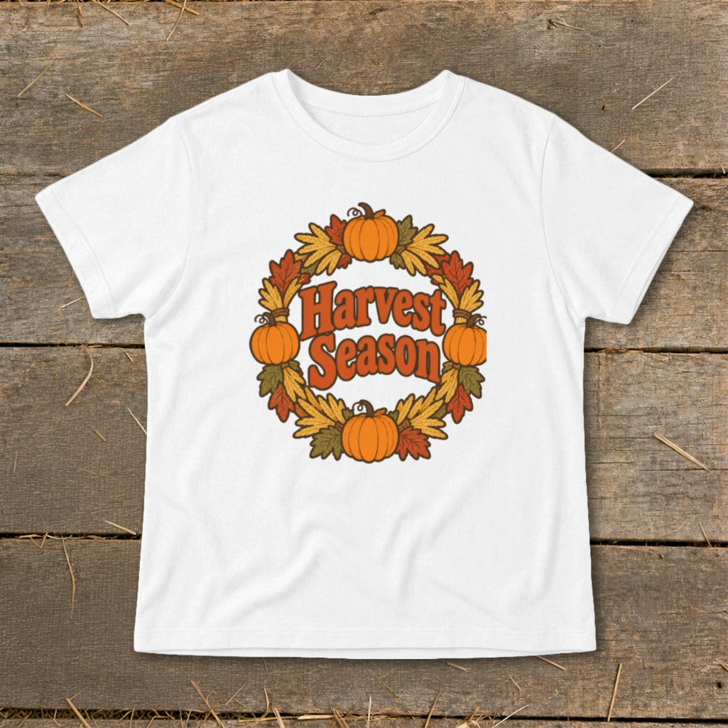 White t-shirt with "Harvest Season" text surrounded by a pumpkin and fall leaf wreath.