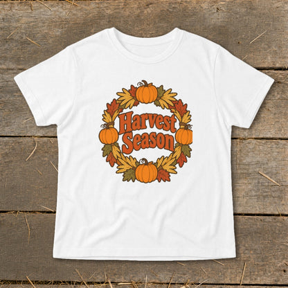 White t-shirt with "Harvest Season" text surrounded by a pumpkin and fall leaf wreath.