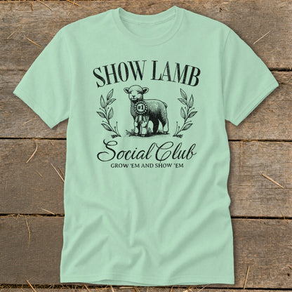 Light green t-shirt with a graphic of a lamb, ribbons, and text: SHOW LAMB SOCIAL CLUB.