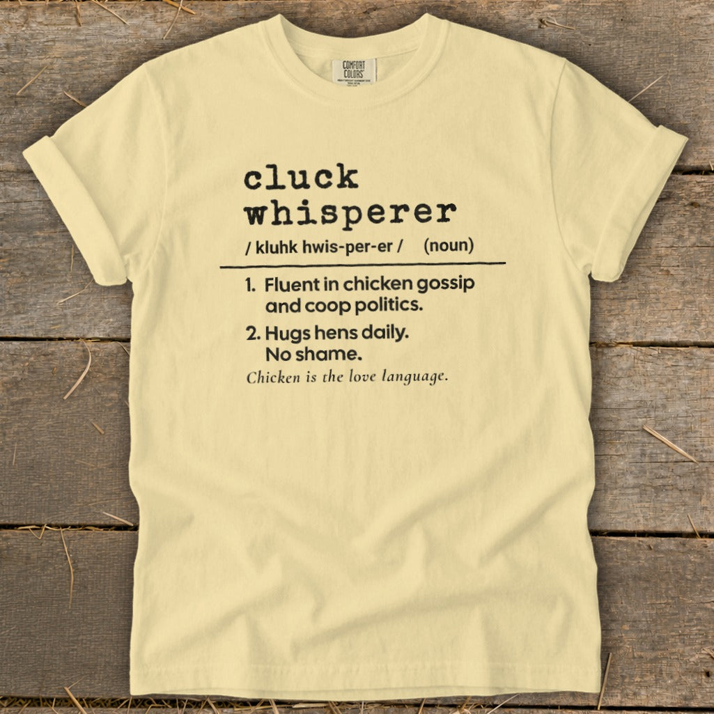 Light yellow t-shirt with "cluck whisperer" definition printed on it.