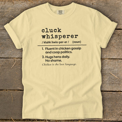Light yellow t-shirt with "cluck whisperer" definition printed on it.