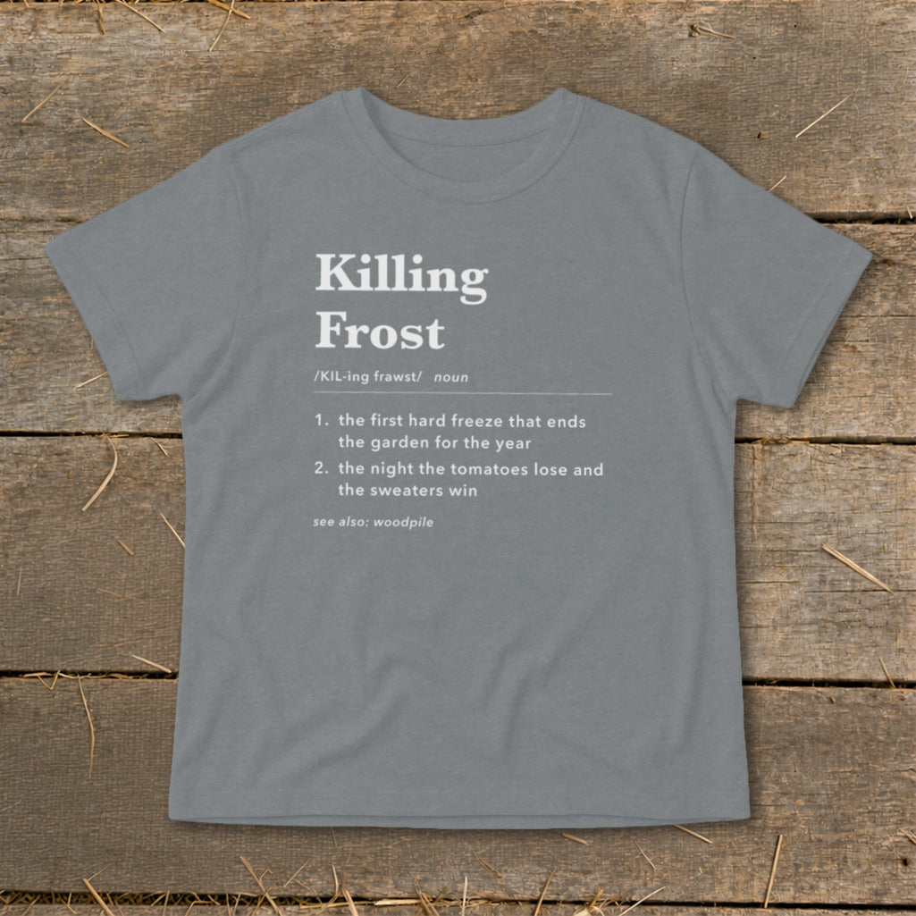 A grey short-sleeve t-shirt with white text defining the term Killing Frost lies on a wooden surface.