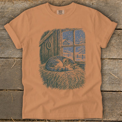 T-shirt with illustration of a cat sleeping on hay in a barn during snowfall.