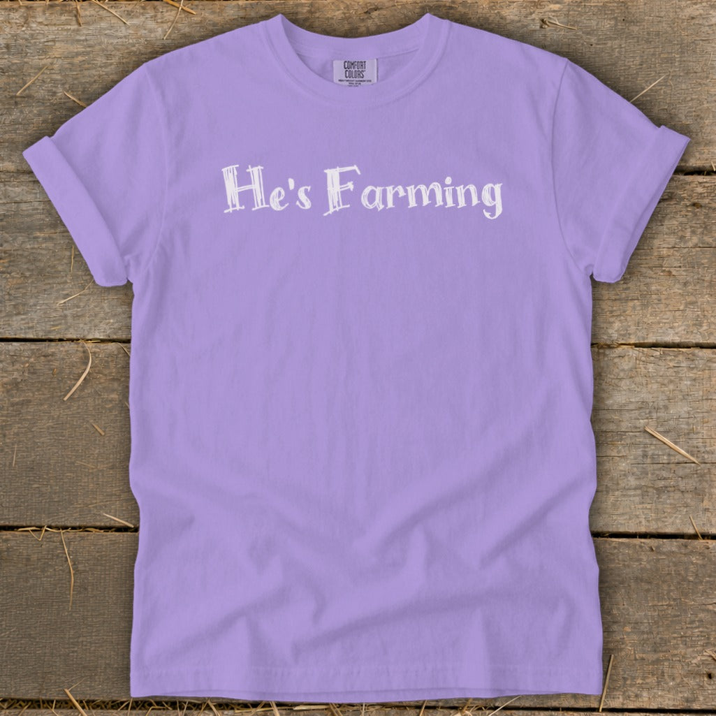 Purple t-shirt with "He's Farming" text on a wooden background.