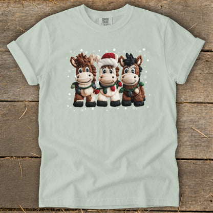 Three cartoon horses with Christmas decorations and a Santa hat, with snowflakes.