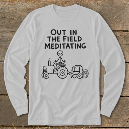 White long-sleeve shirt with text "OUT IN THE FIELD MEDITATING" and a stick figure meditating on a tractor.
