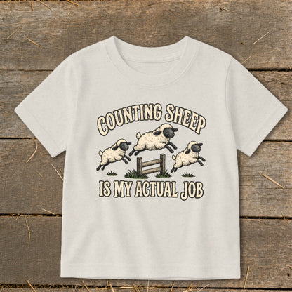 T-shirt with graphic of three sheep jumping over a fence, text reads "Counting Sheep Is My Actual Job."