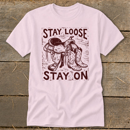 Pink t-shirt with distressed graphic of a saddle and boots, saying "STAY LOOSE STAY ON".