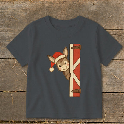 A cute donkey wearing a Santa hat peeks from behind a barn door.