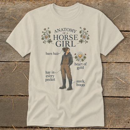 Cream t-shirt with "Anatomy of a Horse Girl" graphic detailing barn hair, hay, and muck boots.