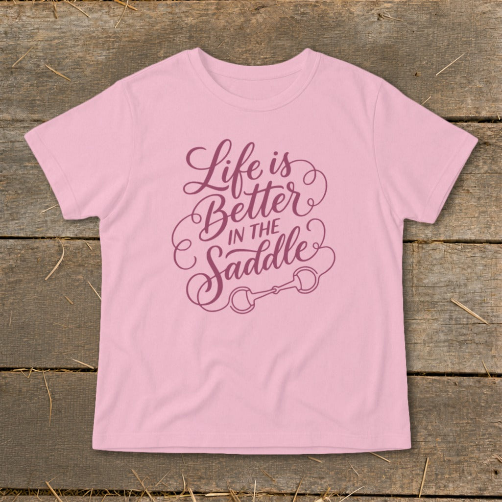 Pink t-shirt with purple text reading "Life is Better in The Saddle" and a horse bit graphic.