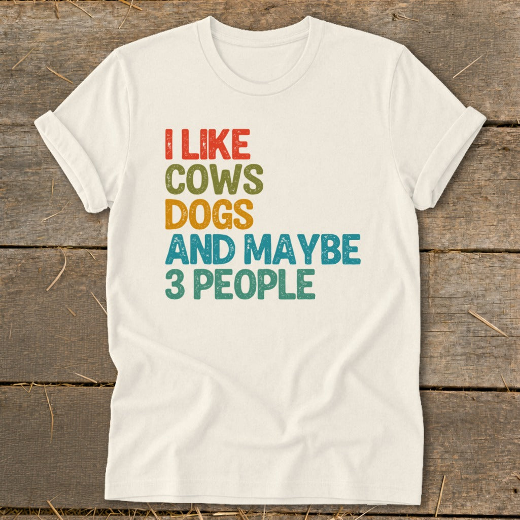 Cream t-shirt with text "I LIKE COWS DOGS AND MAYBE 3 PEOPLE" in colored lettering.