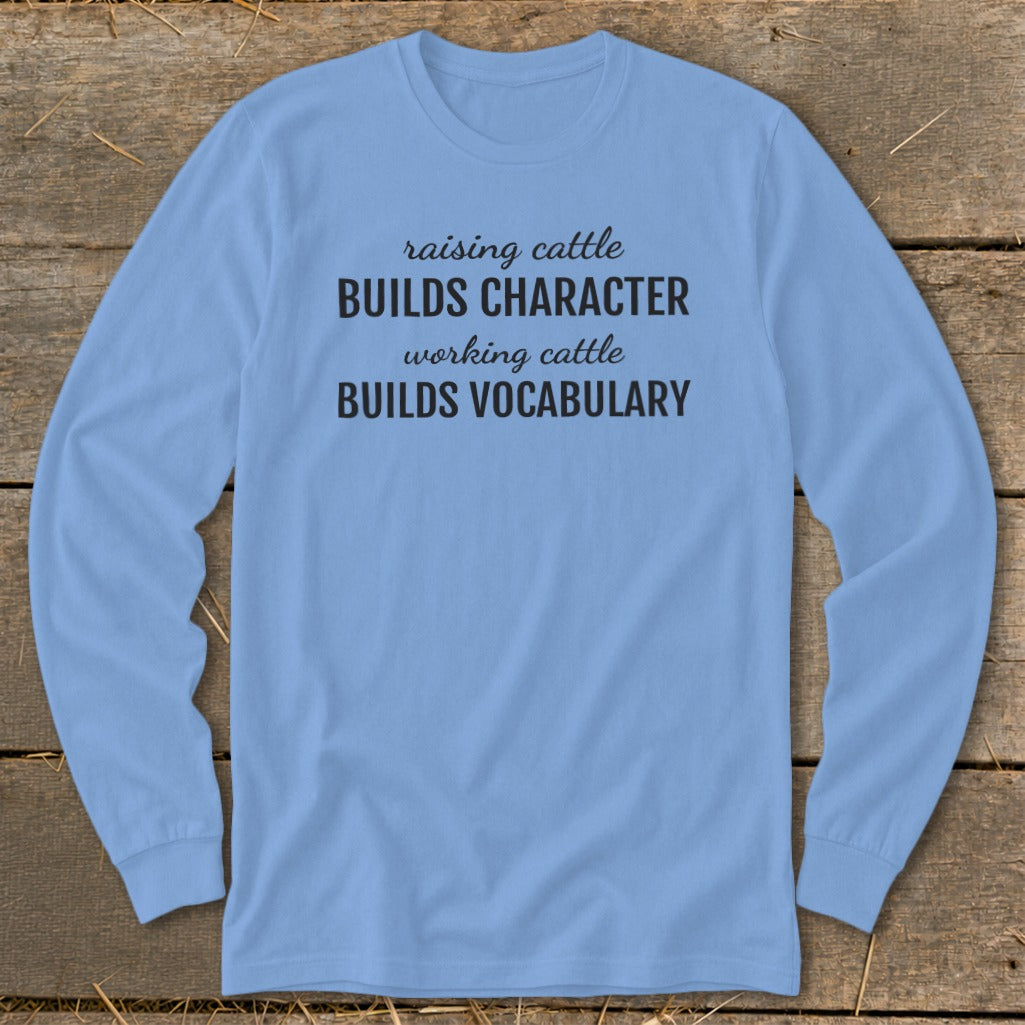 Light blue long-sleeve shirt with text "raising cattle BUILDS CHARACTER working cattle BUILDS VOCABULARY".