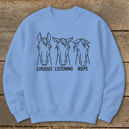 Light blue crewneck sweatshirt featuring three horse head sketches with the captions curious, listening, and nope.