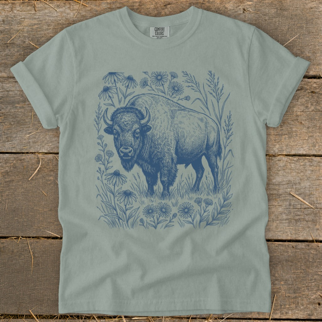 Light blue t-shirt with a dark blue linocut style print of a bison surrounded by wildflowers and grasses.