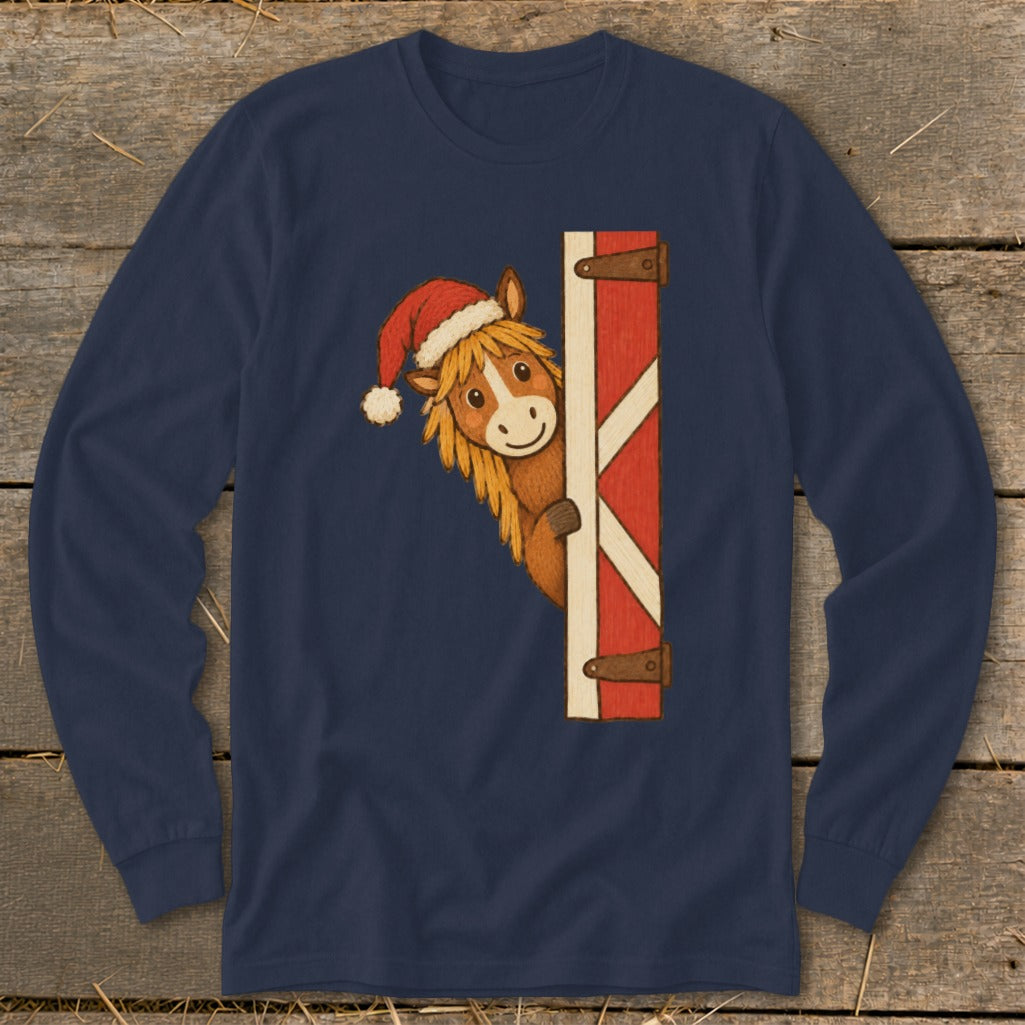 Horse wearing Santa hat peeking from behind red barn door on navy long-sleeve shirt.