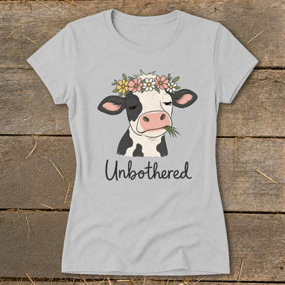 Light gray t-shirt with a cartoon cow wearing a flower crown, eating grass, and text "Unbothered".